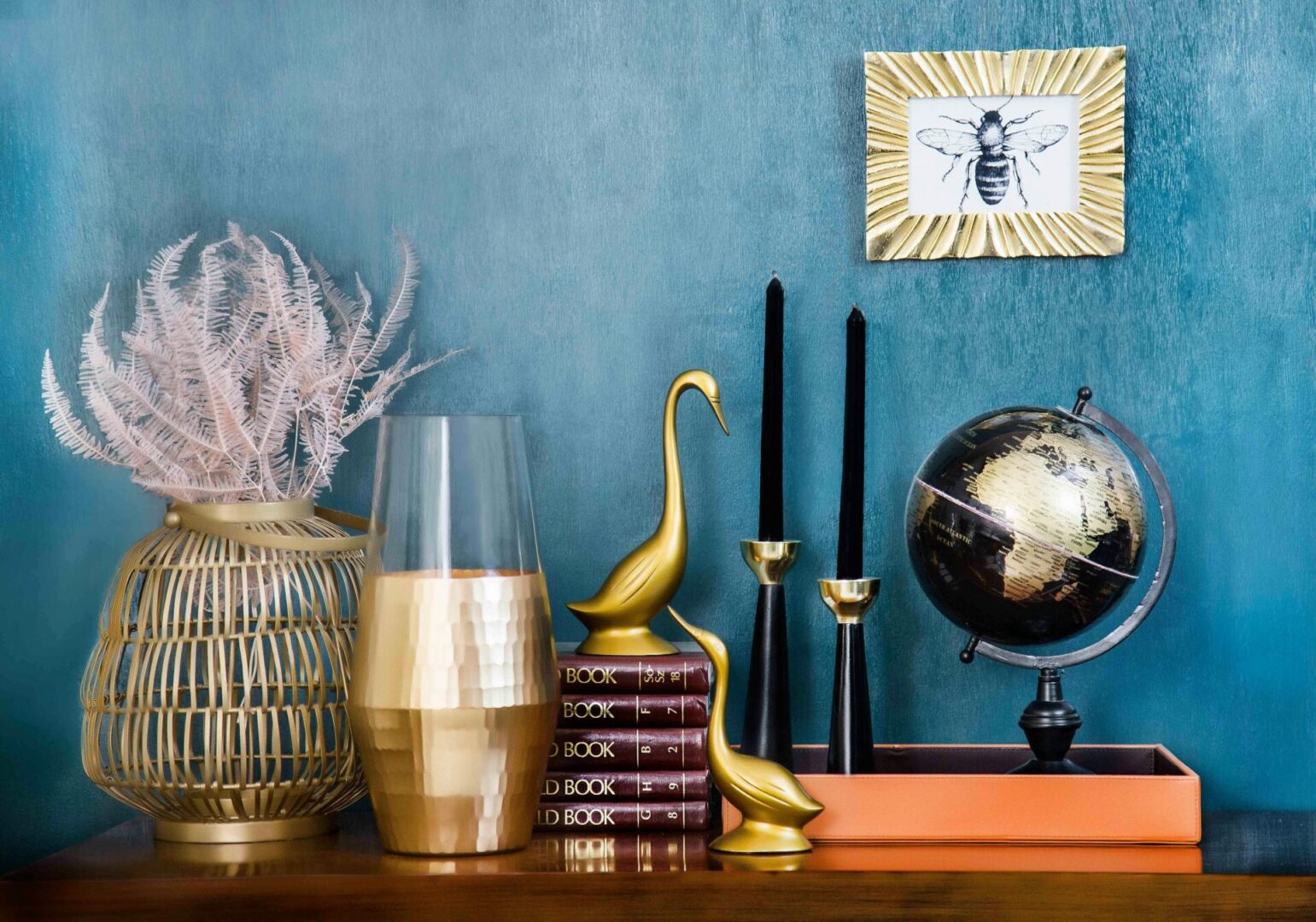 A blue wall with gold vases, books and a globe.